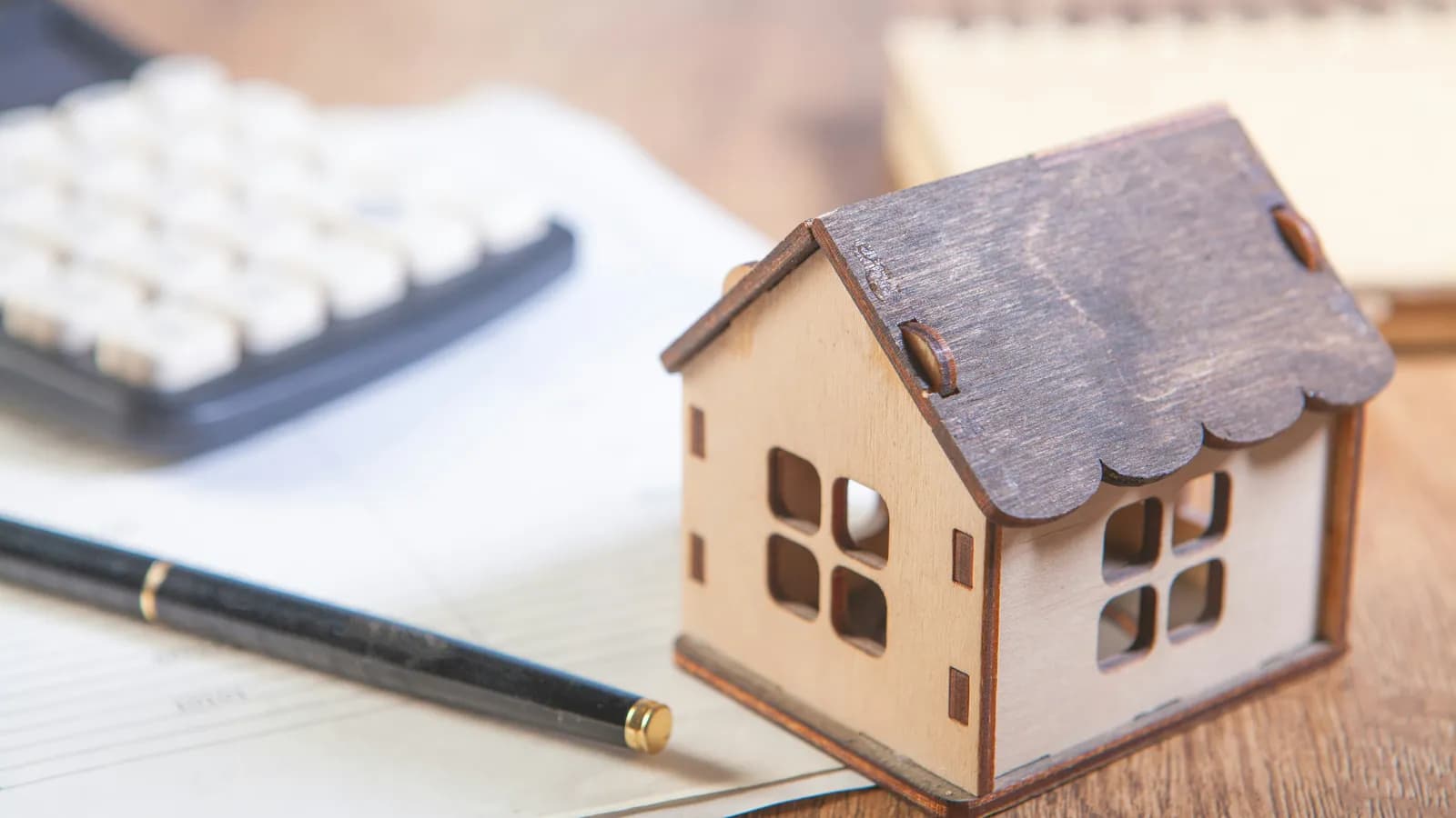 Maison miniature en bois, calculatrice et stylo sur des documents