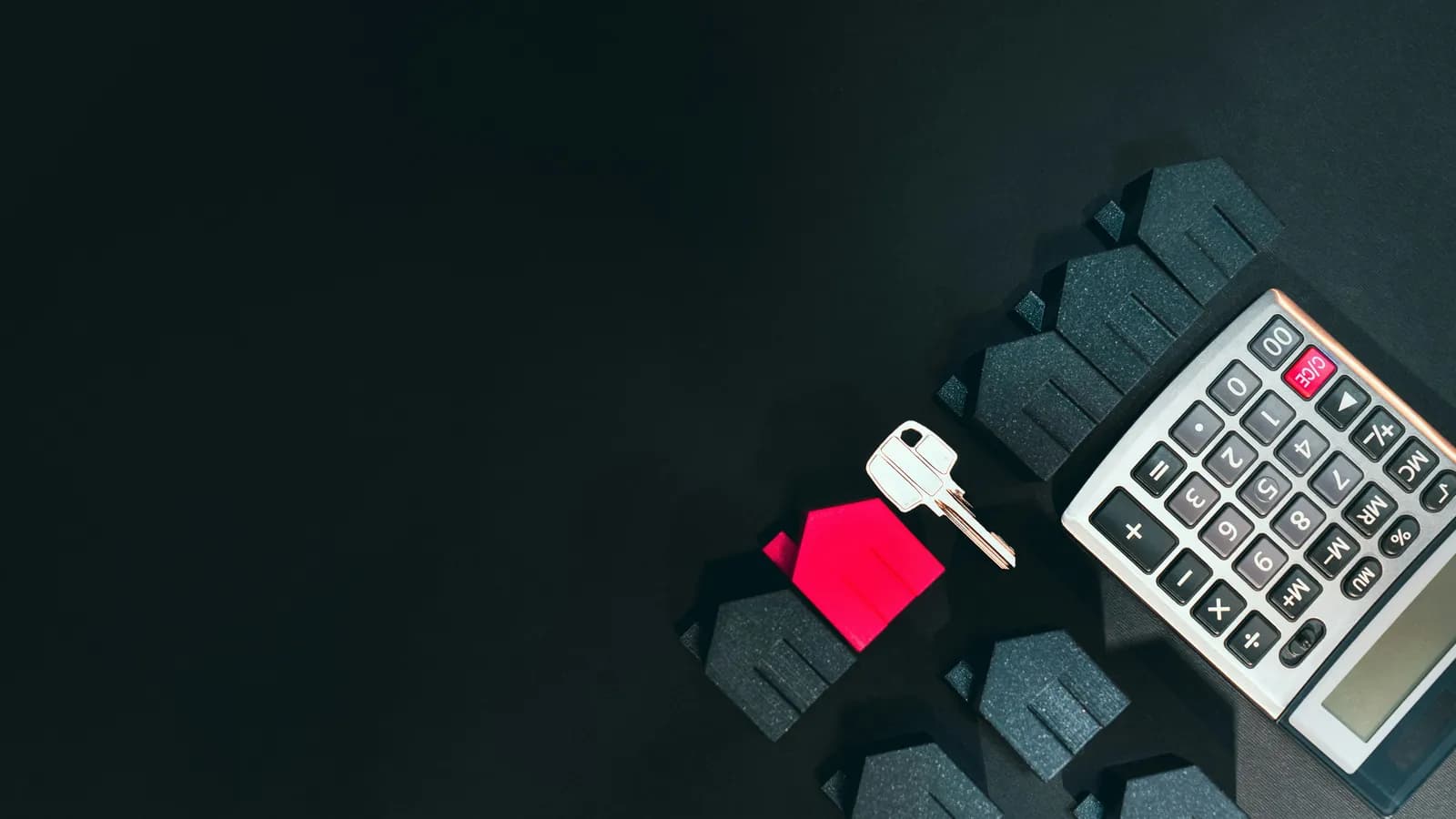 Calculatrice, clé et petite maison rouge sur un bureau sombre