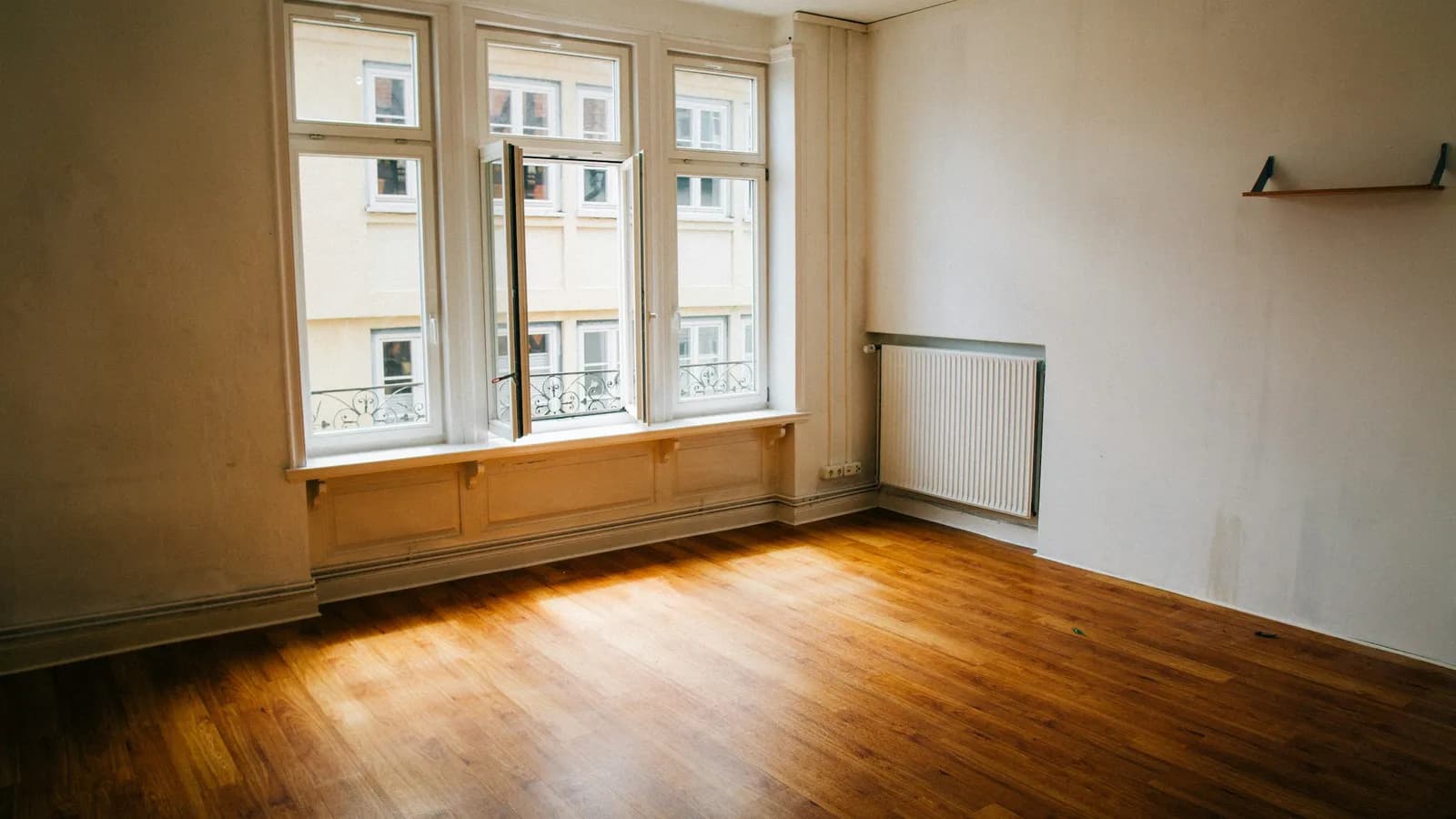 Pièce vide et lumineuse d'un appartement ancien à louer, parquet et grandes fenêtres